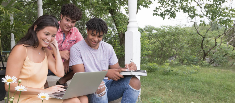 3 people sitting on a porch looking at a laptop