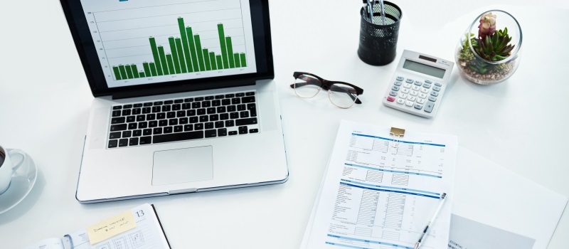 a laptop showing a bar graph, paper notes and supplies on a white desk